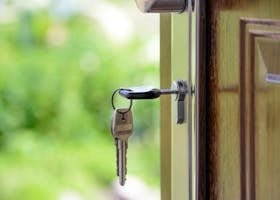 Key inserted in door lock against a blurred green background, symbolizing security and real estate.