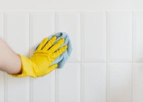A hand in a yellow glove wiping a tiled wall with a cloth, demonstrating cleanliness.