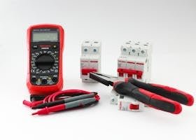 Close-up of a digital multimeter with electrical tools and circuit breakers on a white background.