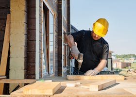 A construction worker using a power drill on a building site, outdoors during the day.